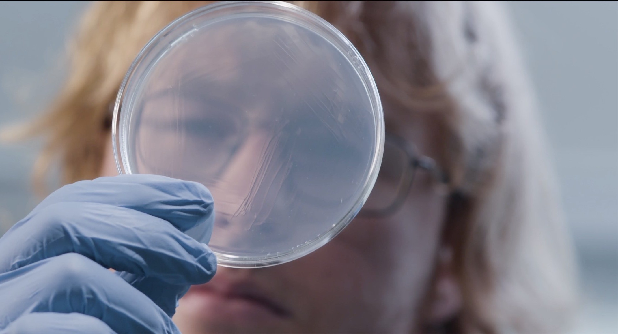 This image shows a female researcher looking through a petri dish .jpg